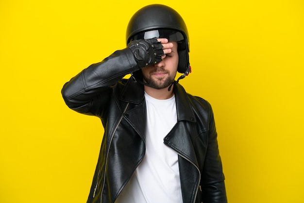 Jovem homem caucasiano com um capacete de motocicleta isolado em fundo amarelo cobrindo os olhos pelas mãos Não quer ver algo