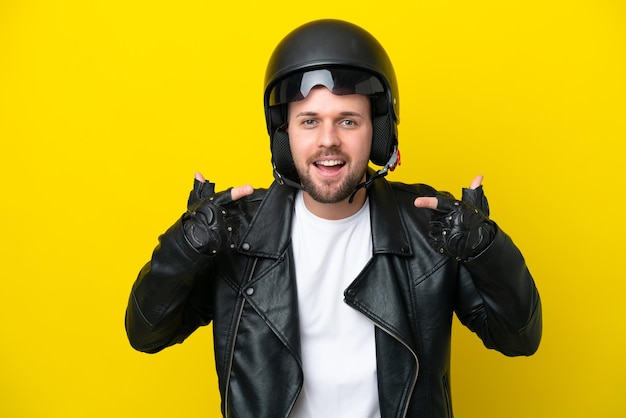 Jovem homem caucasiano com um capacete de motociclista isolado em um fundo amarelo e fazendo um gesto de polegar para cima