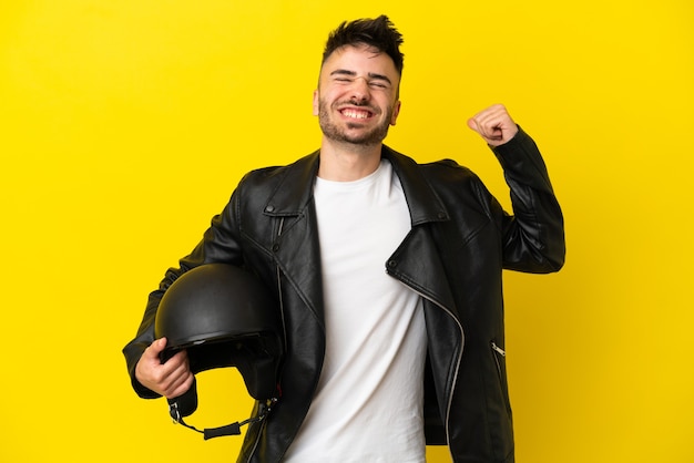 Foto jovem homem caucasiano com um capacete de motociclista isolado em um fundo amarelo fazendo um gesto forte