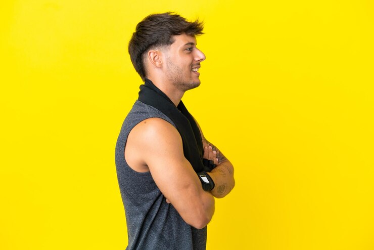 Foto jovem homem caucasiano com uma toalha isolada em um fundo amarelo na posição lateral