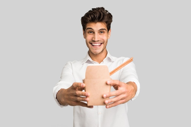 Jovem homem caucasiano comendo um macarrão para viagem isolado