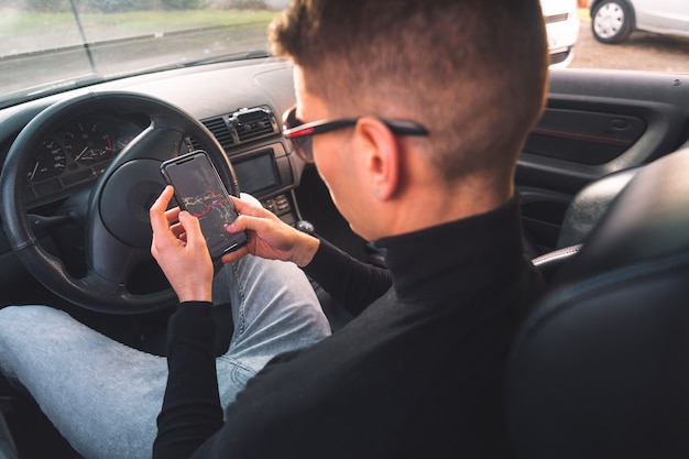 Jovem homem caucasiano dentro de um carro usando um smartphone