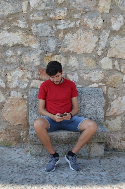 Jovem homem caucasiano em camiseta vermelha usando seu smartphone