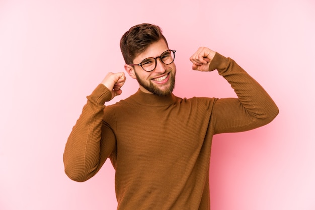 Jovem homem caucasiano em rosa comemorando um dia especial, pula e levanta os braços com energia.