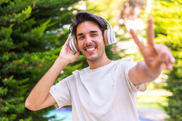 Jovem homem caucasiano em um parque ouvindo música e cantando