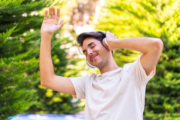 Jovem homem caucasiano em um parque ouvindo música e dançando