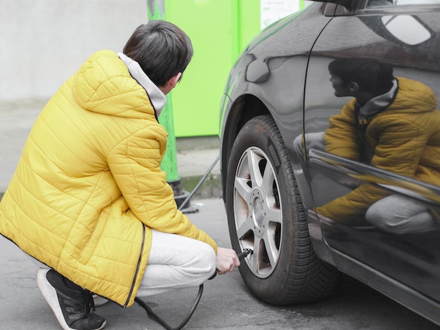 Jovem homem caucasiano em uma jaqueta amarela e calça de moletom cinza agachada bombeando um pneu