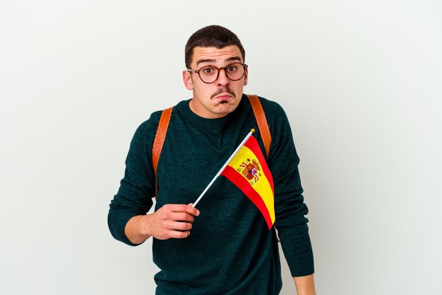 Jovem homem caucasiano estudando inglês isolado no branco encolhe os ombros e abre os olhos confusos.