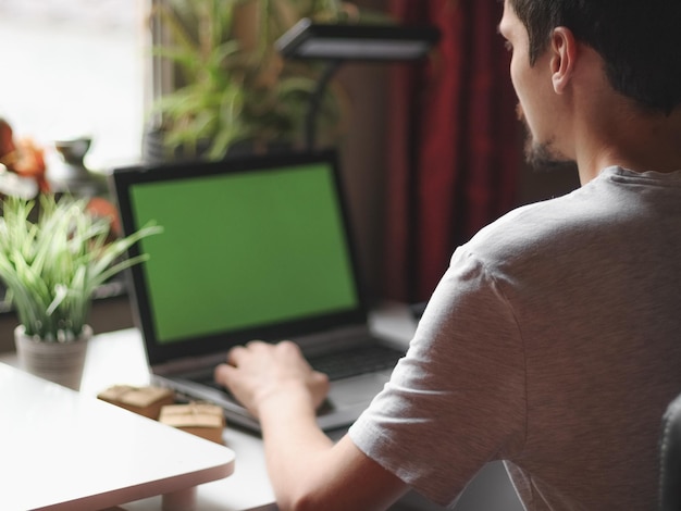 Jovem homem caucasiano fazendo compras onlinesentado em seu quarto com um laptop de tela verde