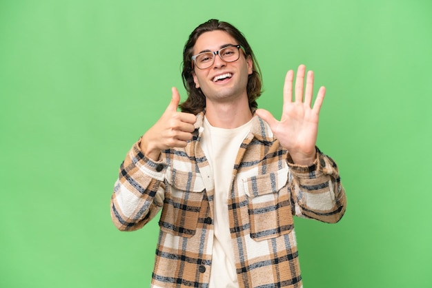 Foto jovem homem caucasiano isolado em croma verde contando seis com os dedos