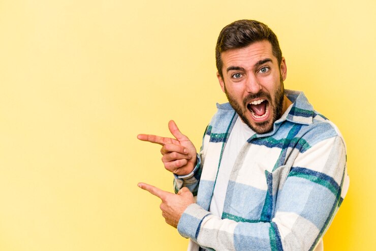 Foto jovem homem caucasiano isolado em fundo amarelo apontando com os dedos indicadores para um espaço de cópia expressando emoção e desejo