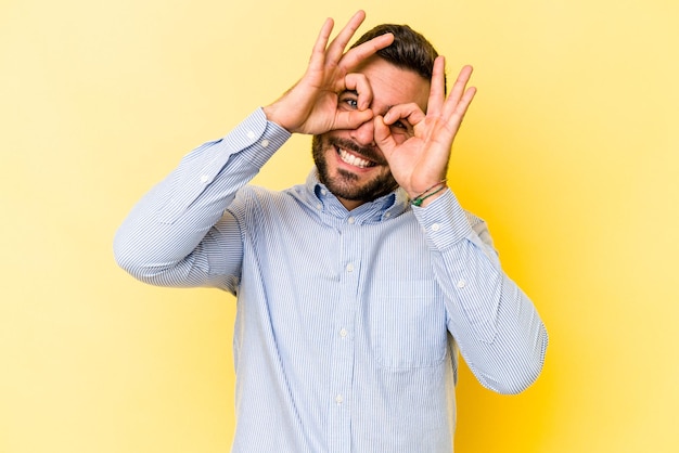 Jovem homem caucasiano isolado em fundo amarelo mostrando sinal de ok sobre os olhos