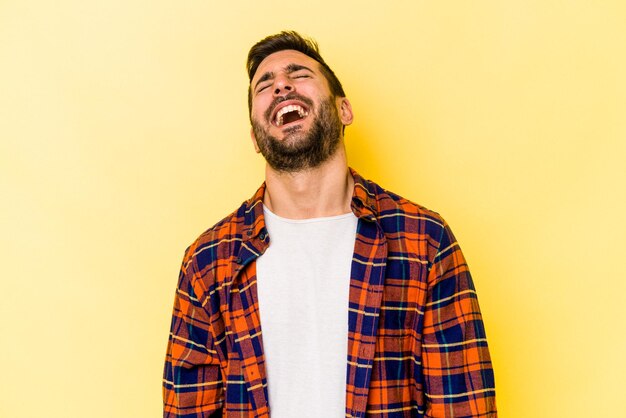 Jovem homem caucasiano isolado em fundo amarelo relaxado e feliz rindo pescoço esticado mostrando os dentes