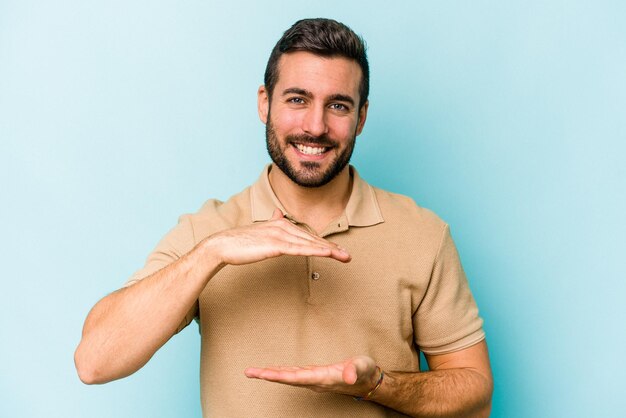 Jovem homem caucasiano isolado em fundo azul segurando algo com ambas as mãos apresentação do produto