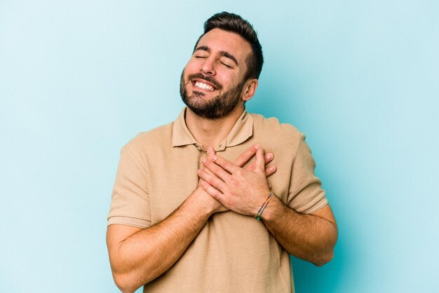 Jovem homem caucasiano isolado em fundo azul tem expressão amigável pressionando a palma da mão no peito Conceito de amor