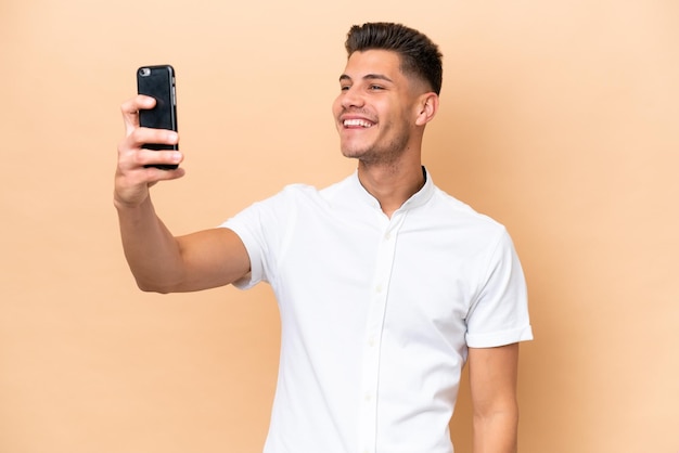 Jovem homem caucasiano isolado em fundo bege, fazendo uma selfie