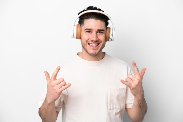 Jovem homem caucasiano isolado em fundo branco ouvindo música fazendo gesto de rock