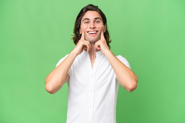 Jovem homem caucasiano isolado em fundo croma verde sorrindo com uma expressão feliz e agradável