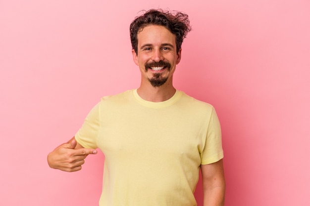 Jovem homem caucasiano isolado em fundo rosa pessoa apontando com a mão para um espaço de cópia de camisa, orgulhoso e confiante