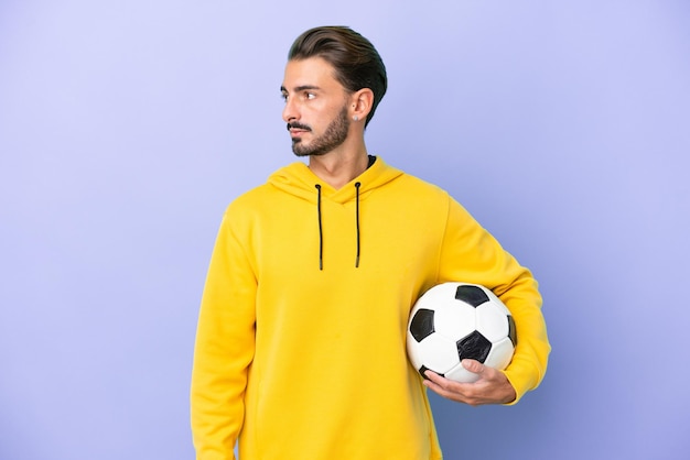 Jovem homem caucasiano isolado em fundo roxo com bola de futebol