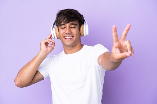 Jovem homem caucasiano isolado em fundo roxo ouvindo música e cantando