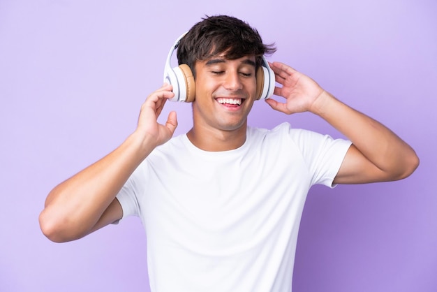 Jovem homem caucasiano isolado em fundo roxo ouvindo música e cantando