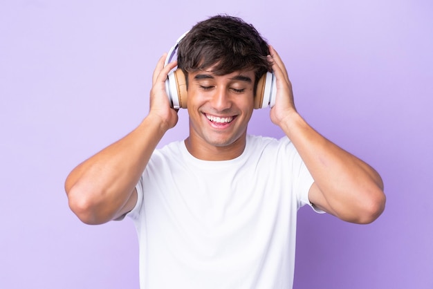 Jovem homem caucasiano isolado em fundo roxo ouvindo música