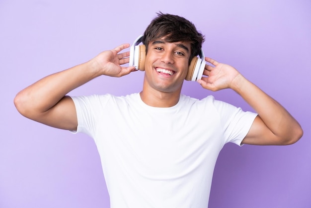 Jovem homem caucasiano isolado em fundo roxo ouvindo música