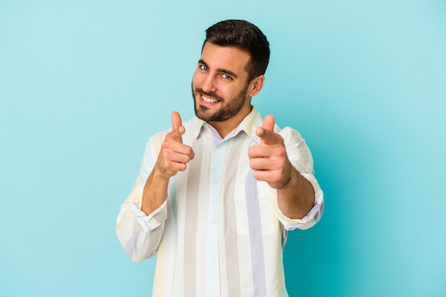 Jovem homem caucasiano isolado em sorrisos alegres de parede azul, apontando para a frente.