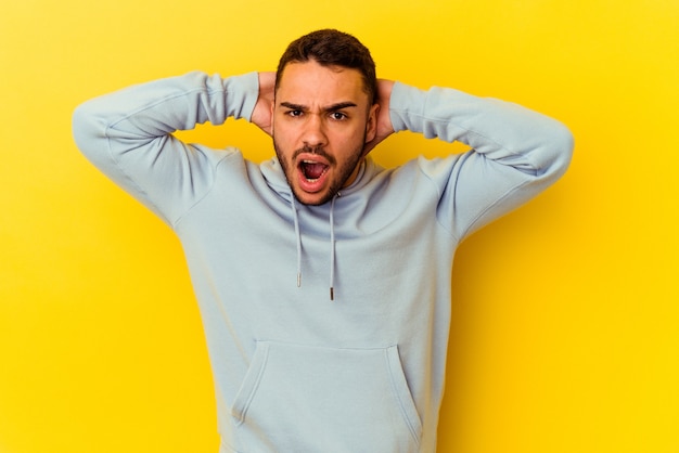 Jovem homem caucasiano isolado em um fundo amarelo, gritando de raiva.