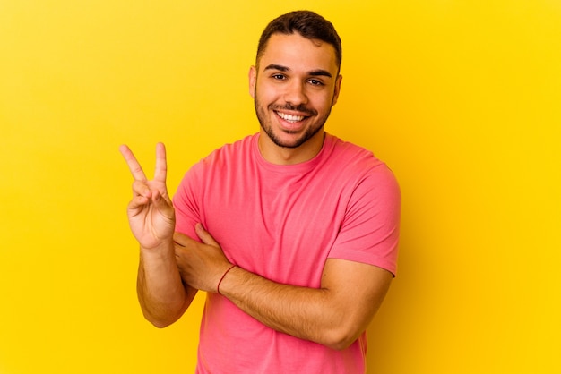 Jovem homem caucasiano isolado em um fundo amarelo, mostrando o número dois com os dedos.