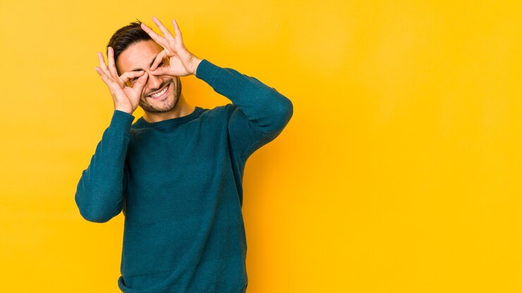 Foto jovem homem caucasiano isolado em um fundo amarelo mostrando sinal de aprovação sobre os olhos
