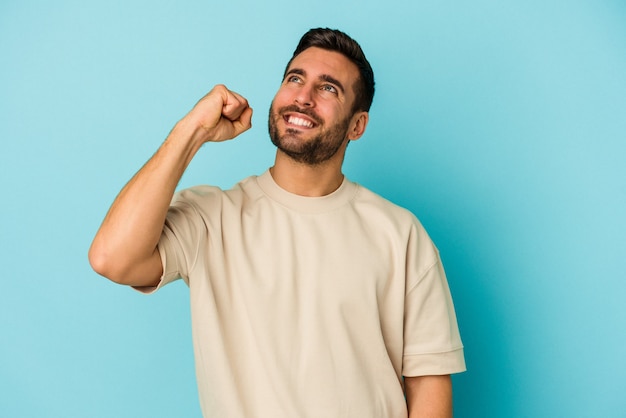 Jovem homem caucasiano isolado em um fundo azul, comemorando uma vitória, paixão e entusiasmo, expressão feliz.