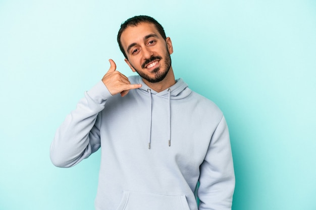 Jovem homem caucasiano isolado em um fundo azul, mostrando um gesto de chamada de celular com os dedos.