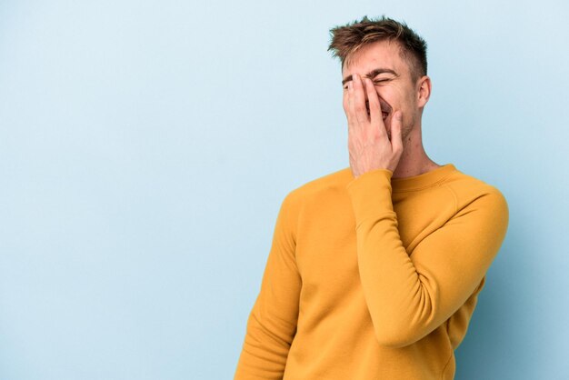 Jovem homem caucasiano isolado em um fundo azul, rindo de emoção feliz, despreocupada e natural.