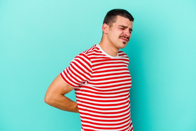 Jovem homem caucasiano isolado em um fundo azul, sofrendo de dor nas costas.