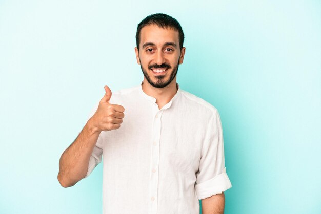 Jovem homem caucasiano isolado em um fundo azul, sorrindo e levantando o polegar