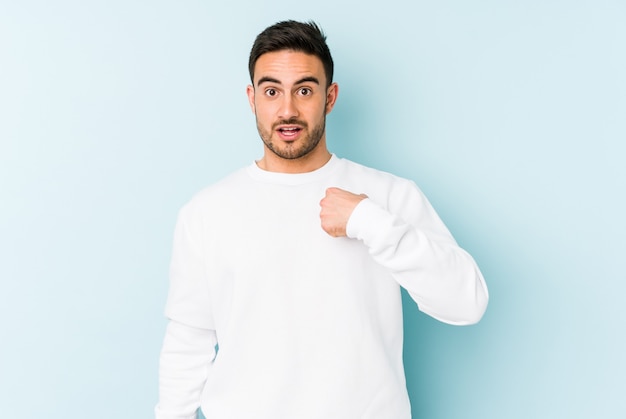 Jovem homem caucasiano isolado em um fundo azul surpreendido apontando com o dedo, sorrindo amplamente.