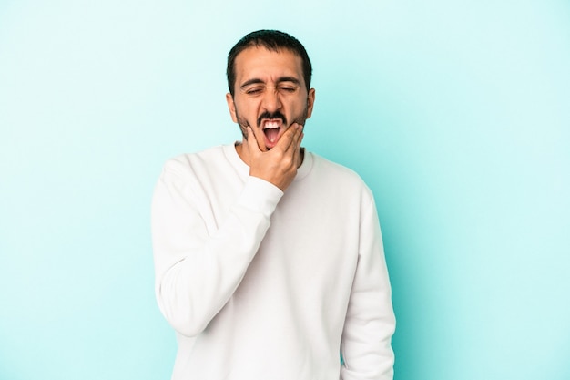 Jovem homem caucasiano isolado em um fundo azul, tendo uma forte dor nos dentes, dor molar.