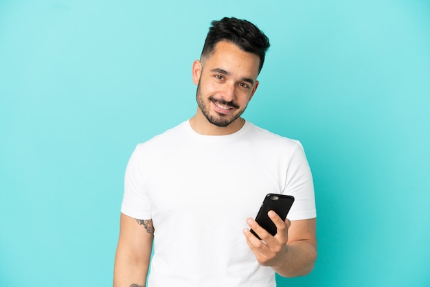 Jovem homem caucasiano isolado em um fundo azul usando telefone celular