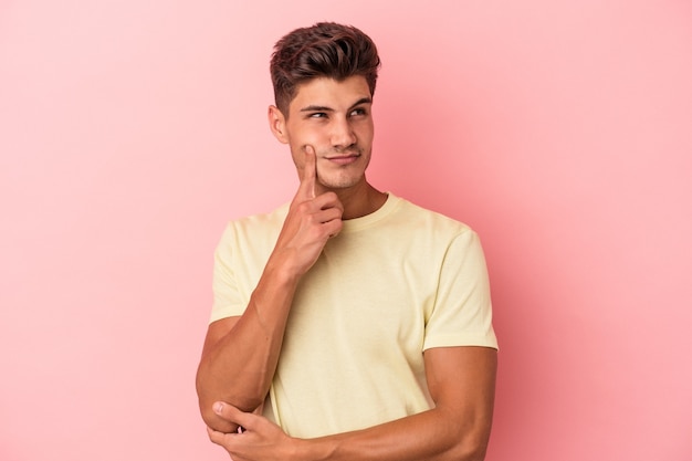 Jovem homem caucasiano isolado em um fundo rosa, contemplando, planejando uma estratégia, pensando na forma de um negócio.