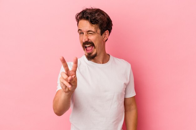 Jovem homem caucasiano isolado em um fundo rosa, mostrando o número dois com os dedos.