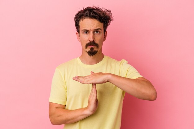 Jovem homem caucasiano isolado em um fundo rosa, mostrando um gesto de tempo limite.