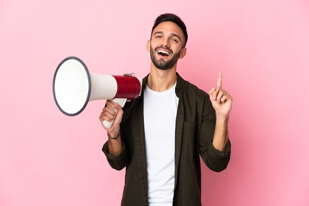 Jovem homem caucasiano isolado em um fundo rosa segurando um megafone e apontando uma ótima ideia