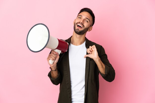 Jovem homem caucasiano isolado em um fundo rosa segurando um megafone e orgulhoso e satisfeito consigo mesmo