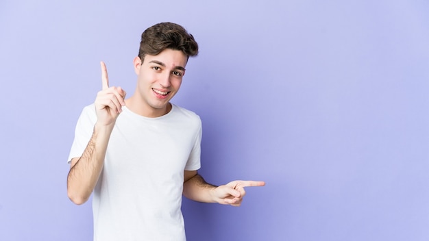 Jovem homem caucasiano isolado em um fundo roxo, apontando para diferentes espaços de cópia, escolhendo um deles, mostrando com o dedo.