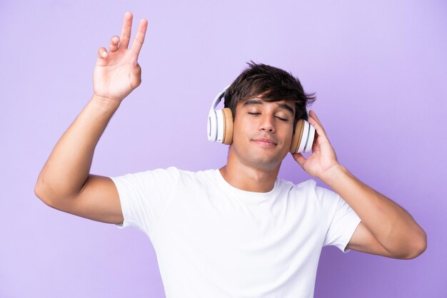 Jovem homem caucasiano isolado em um fundo roxo ouvindo música e dançando