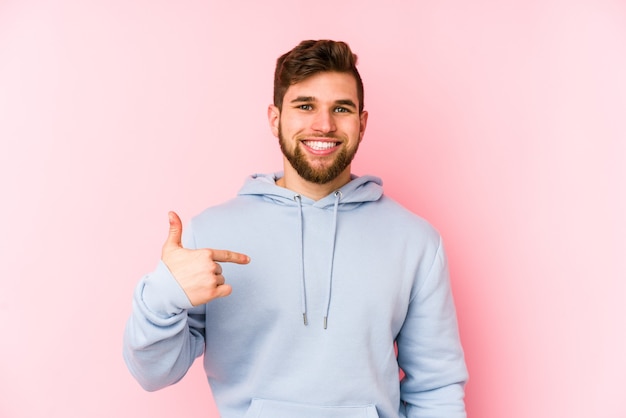 Jovem homem caucasiano isolado em uma pessoa rosa apontando com a mão para um espaço de cópia de camisa, orgulhoso e confiante