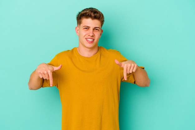 Jovem homem caucasiano isolado na parede azul apontando para baixo com os dedos, sentimento positivo