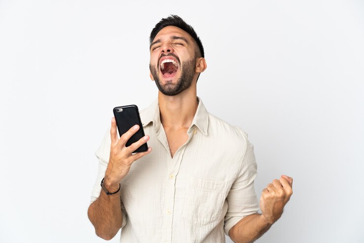 Foto jovem homem caucasiano isolado na parede branca usando telefone celular e fazendo gesto de vitória